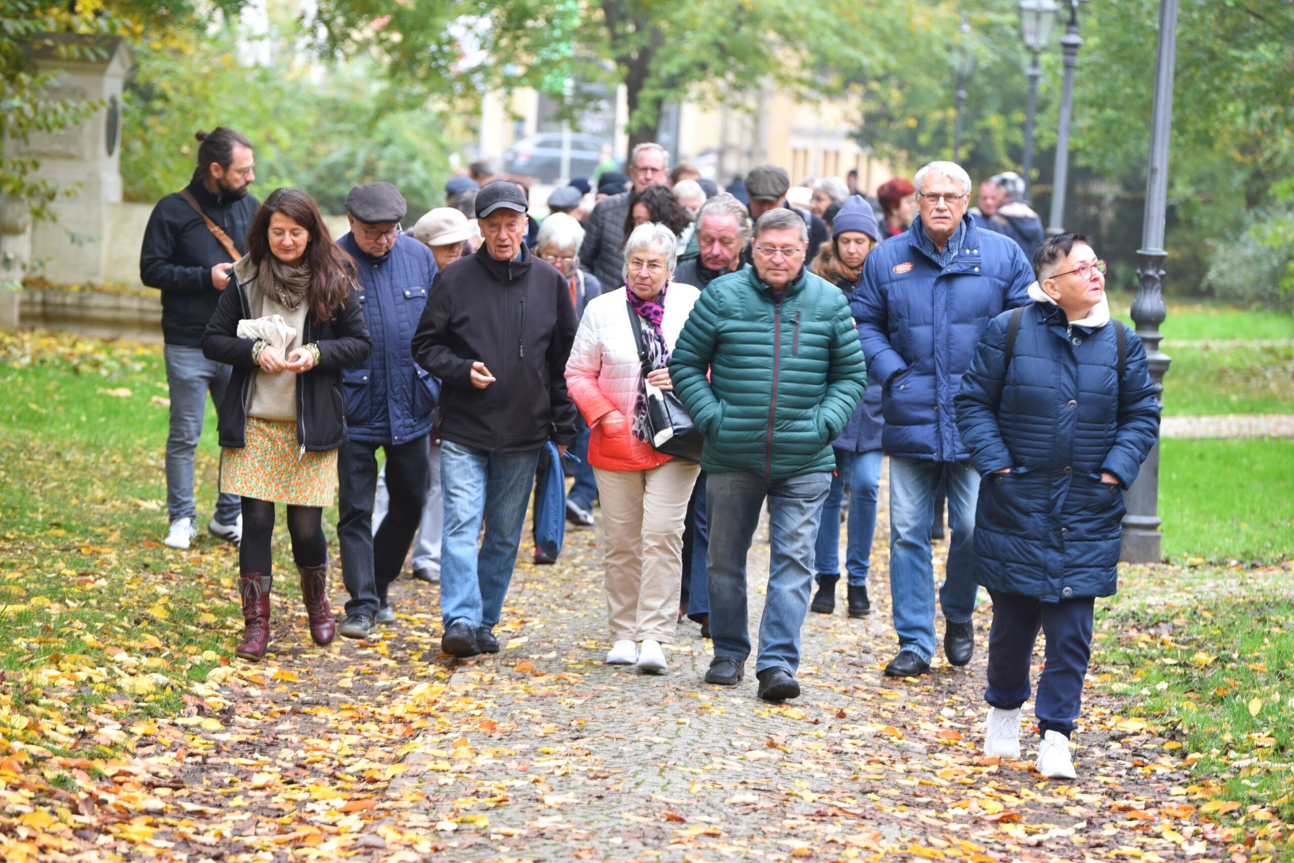 Eine Gruppe Menschen läuft bei herbstlichem Wetter durch eine Parkanlage.
